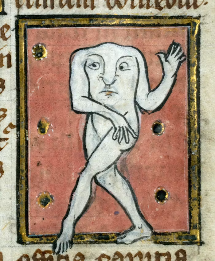 A medieval manuscript illustration within a gold-bordered rectangular frame, featuring a Blemmyes, a mythical, headless human-like figure. Its face is depicted on its chest, with two large eyes, a prominent nose, and a small mouth. Its arms emerge from either side of its head-chest, with one hand raised and open, and the other resting on its hip. The legs are crossed as if walking or dancing. The figure's skin is pale, almost white. The background within the frame is a muted reddish-pink with four scattered gold circular accents. The overall style is characteristic of medieval illumination [gen AI description].